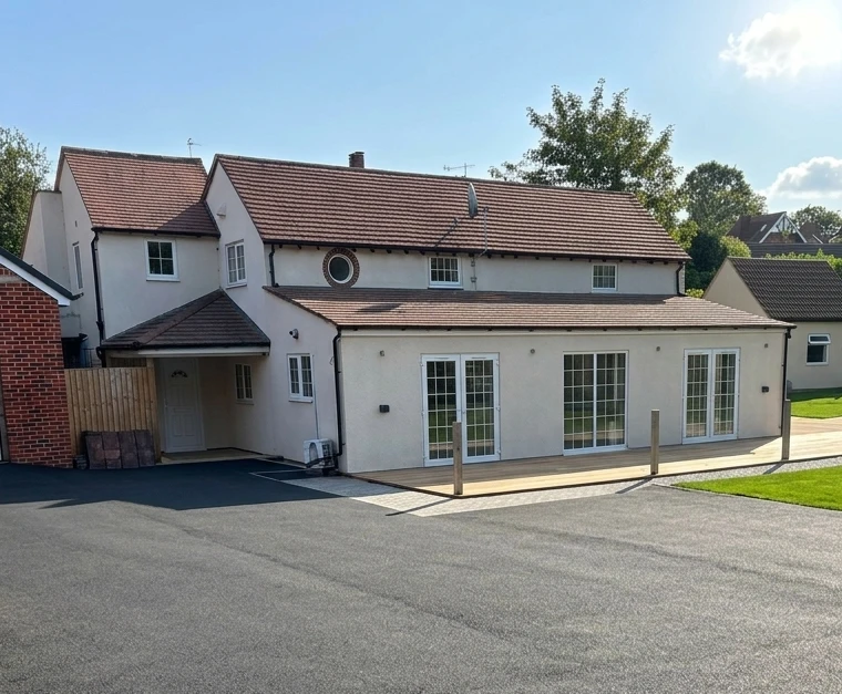 Spinney Cottage from the driveway: a rendered two-storey house with a tiled roof, a porch to the left and three sets of French doors opening onto a patio.